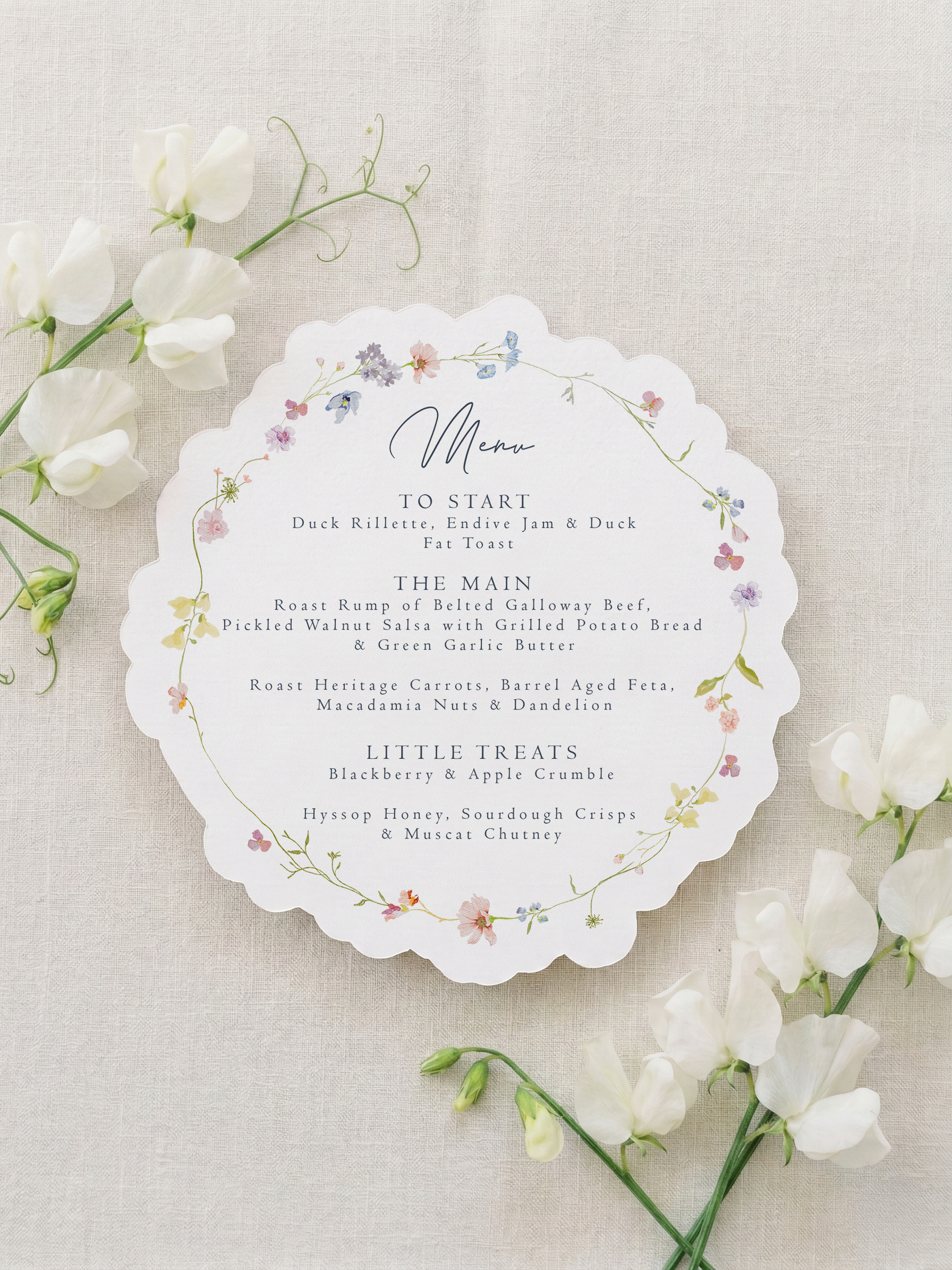 Scalloped botanical wedding menu on natural matte cardstock with a custom guest name tag, gold eyelet, and white silk ribbon