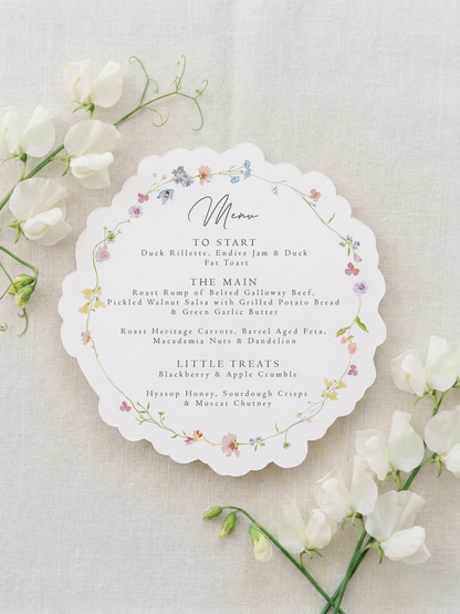 Scalloped botanical wedding menu on natural matte cardstock with a custom guest name tag, gold eyelet, and white silk ribbon