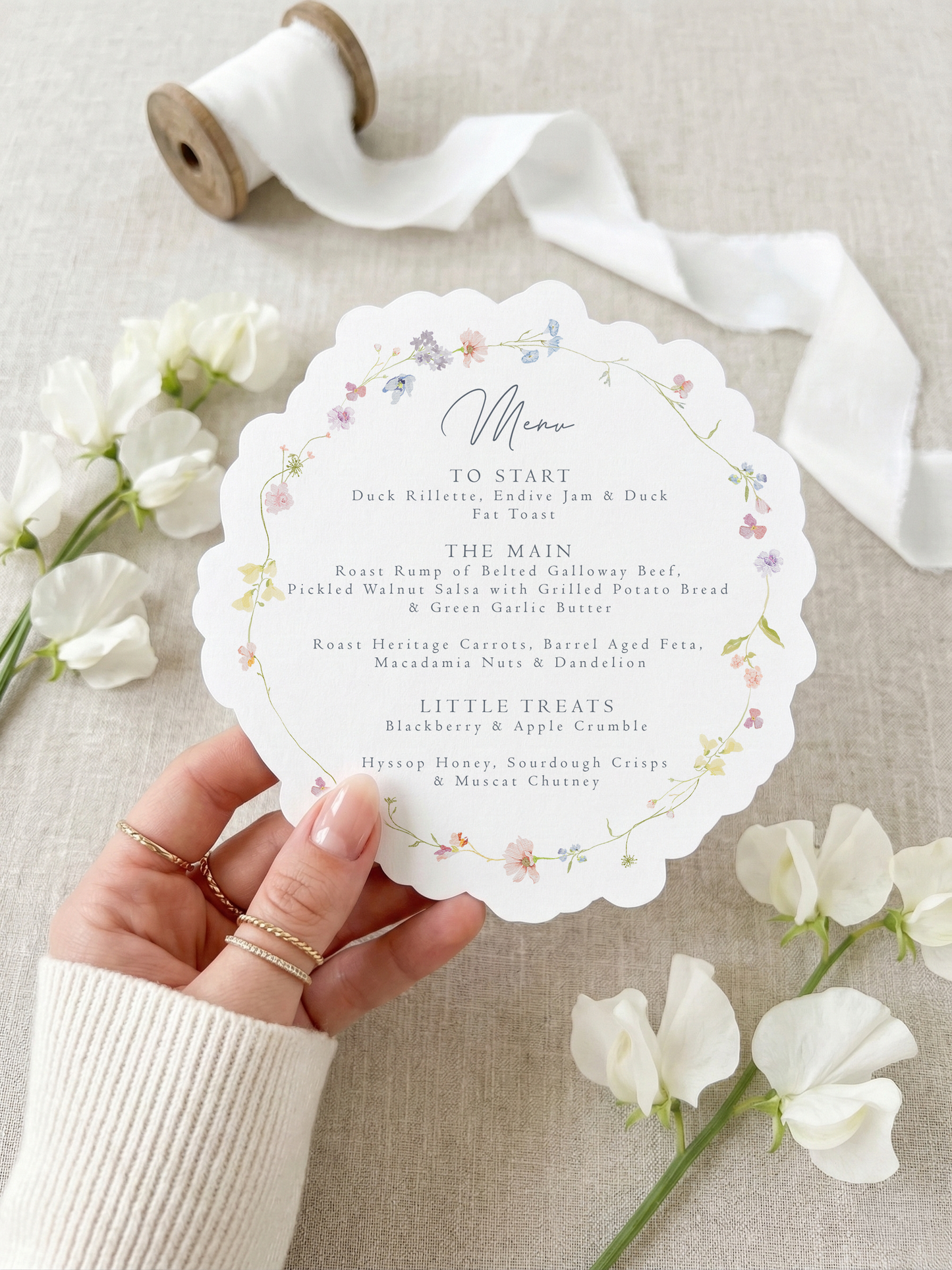 Scalloped botanical wedding menu on natural matte cardstock with a custom guest name tag, gold eyelet, and white silk ribbon